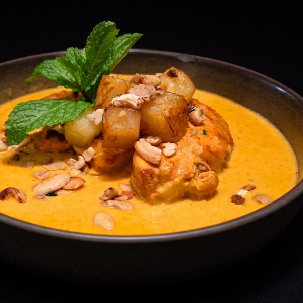 Chicken curry with potatoes, cashews, and mint in a dark bowl against a black background.