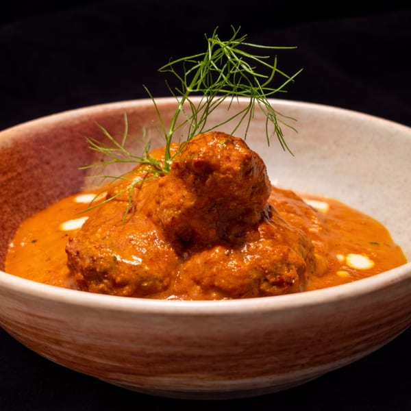 Meatballs in a rich orange sauce, garnished with fresh dill, served in a rustic bowl.
