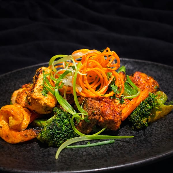 Spiced chicken and paneer with broccoli, carrots, and scallions on a dark plate.