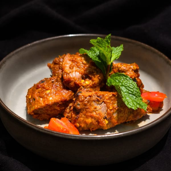 Spicy meat chunks garnished with fresh mint and tomato slices in a rustic bowl.